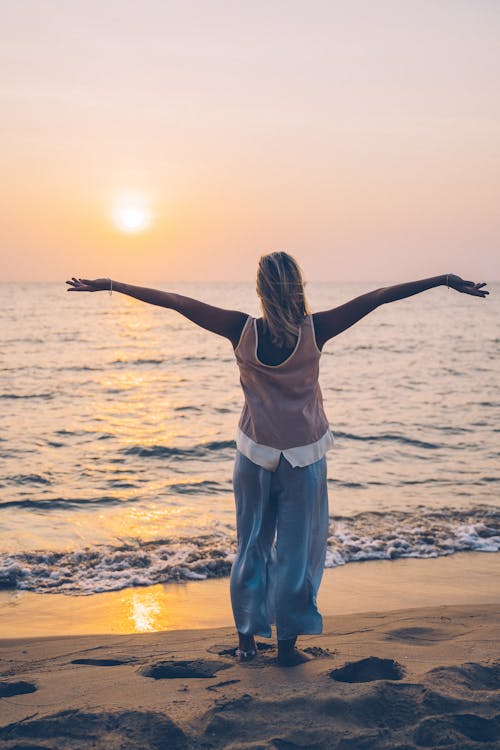 Free A Woman Feeling the Breeze of the Wind while Standing on the Shore of a Beach Stock Photo